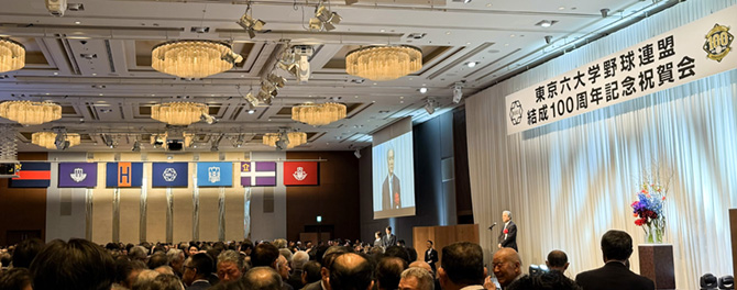 六校の旗の下で乾杯の挨拶をする全塾長の長谷山彰・全日本大学野球連盟会長の写真